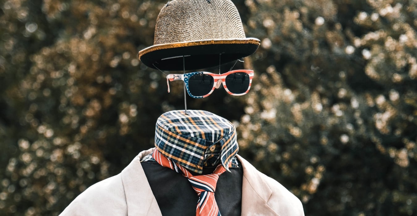 Brand Identity using social media Photo shows faceless figure staning upright in tan suit jacket, black sweater or a plaid button down shirt, a red tie, US flag shades and a hat