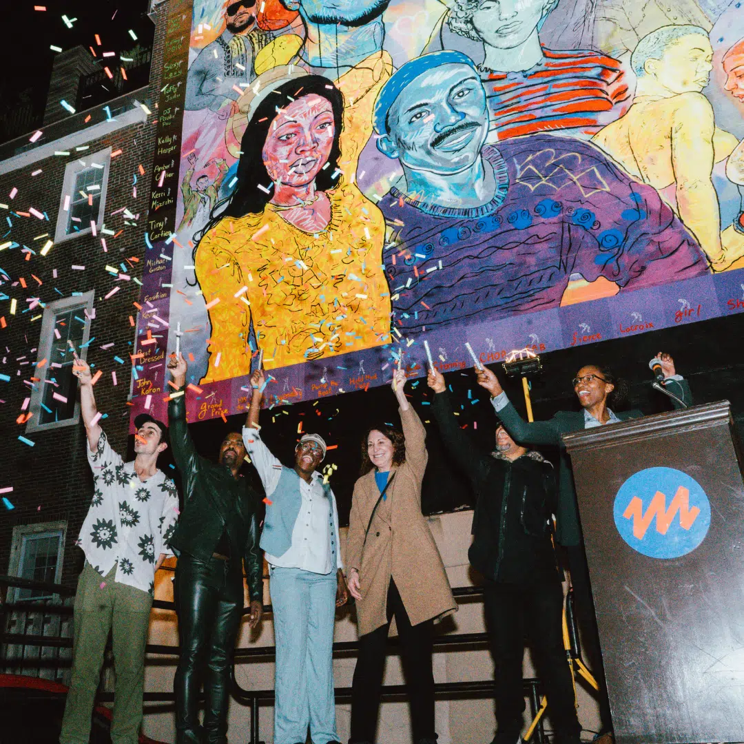 Photo of 5 people including artist Nile Livingston standing in front of the "Finally on 13th” mural celebrating the Philadelphia ballroom scene. Everyone has their hands raised.