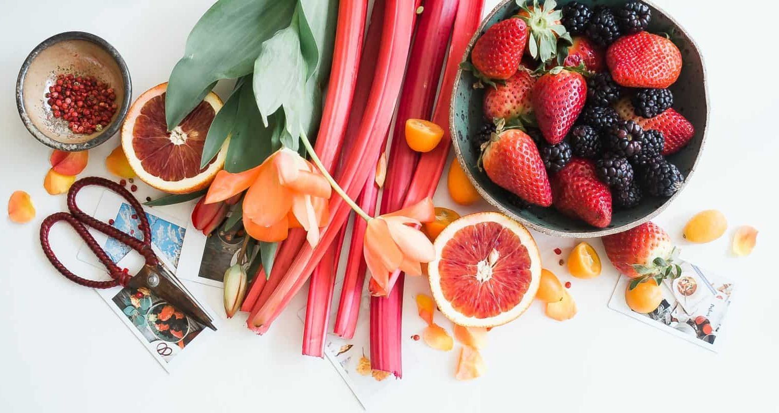 A top down view of various kinds of fruit and a scissor on a table.