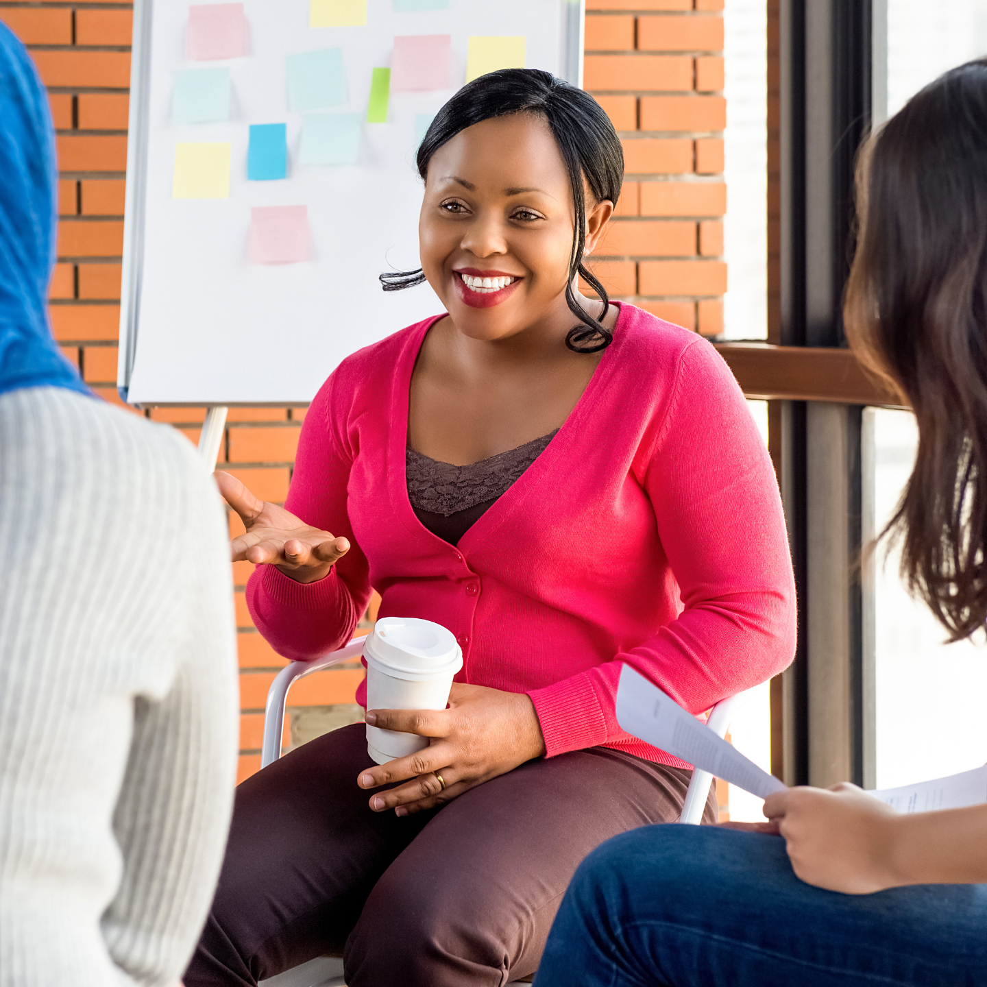 Woman speaking in a small group meeting while holding a coffee cup during a collaborative discussion session.