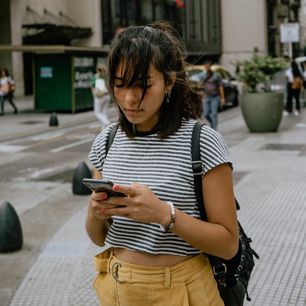 Woman checking her phone while walking on a city sidewalk