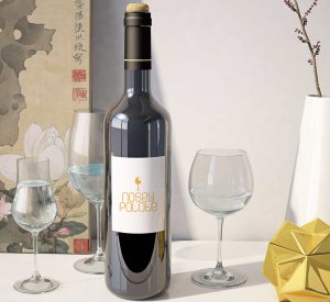 A bottle of wine with the new logo design and branding for Nosey Palate. The wine bottle is in the middle of 2 wine glasses on a white table.